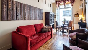 A red sofa, wooden floor, and a dining area with chairs and a table.