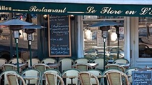 An outdoor seating area with wicker chairs and tables, a chalkboard menu, and a sign indicating the restaurant name.