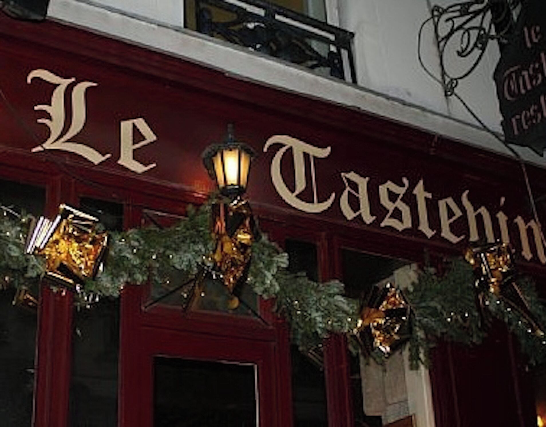 Une façade d’immeuble ornée de l’enseigne « Le Tastehin » et de guirlandes décoratives.