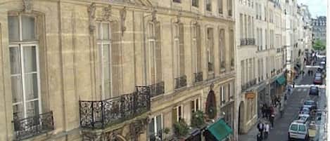 A street view of a historic building with classical architecture, including ornate balconies and detailed stonework.