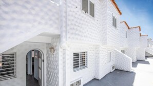Ein weißes Gebäude mit zahlreichen Fenstern und einer Tür, mit einer strukturierten Fassade und einem Ziegeldach.