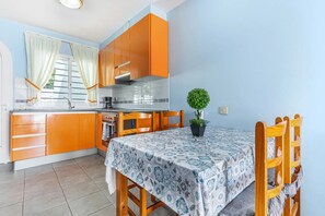 A compact kitchen with orange cabinets, a tiled backsplash, and a dining table with a patterned tablecloth.