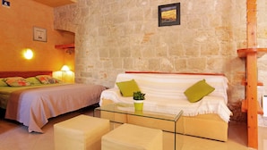 A cozy room with a stone wall, a bed with green pillows, a glass coffee table, and a small plant. - All you need studio apartment in Split city center (Split)