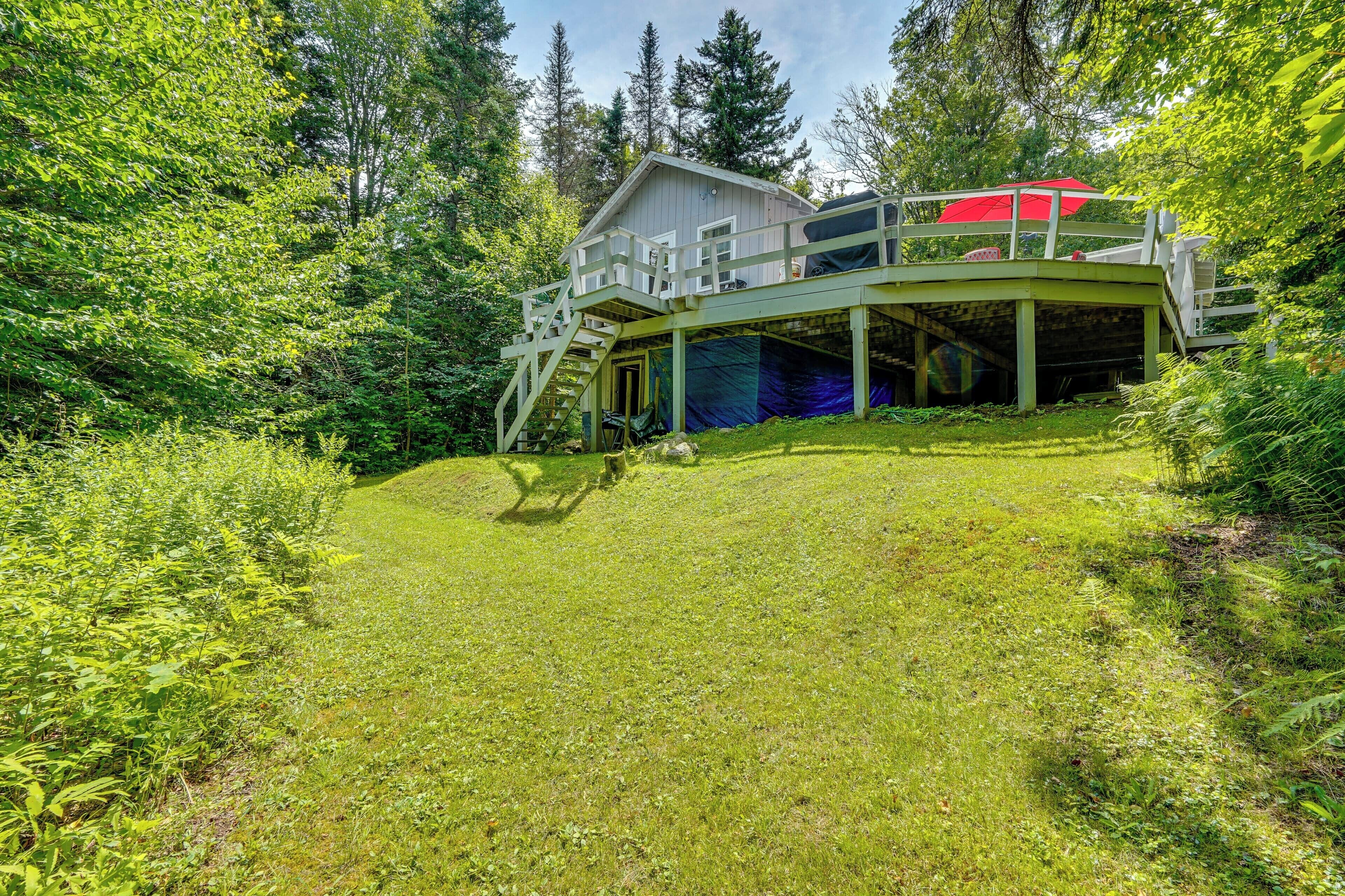 A cabin with a wooden deck and a covered area, surrounded by dense forest.