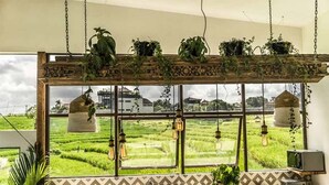 Eine Küche mit einem großen Fenster mit Blick auf ein Reisfeld, einem hängenden Pflanzenregal und einem Vintage-Radio.