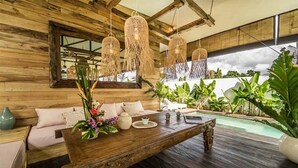 Ein Holzinterieur mit einem Holztisch, hängenden Korblampen und Blick auf einen Pool.