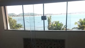 A room with a large window overlooking a coastal area with boats and palm trees. - House Residencia (Búzios)