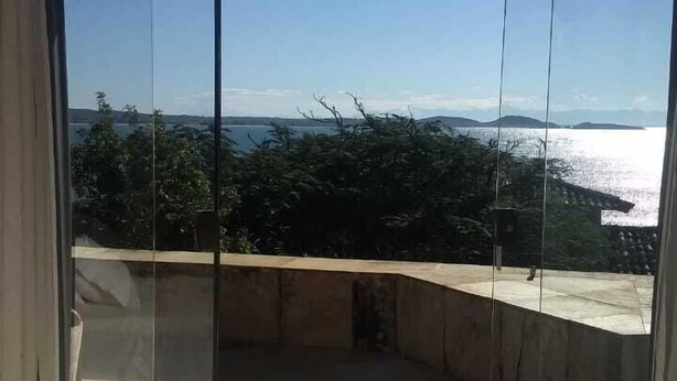 A room with a large sliding glass door leading to a balcony with a view of the sea and hills. - House Residencia (Búzios)