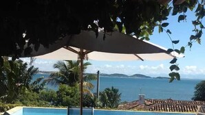 A poolside area with a table and chairs, a large umbrella, and a view of the ocean. - House Residencia (Búzios)