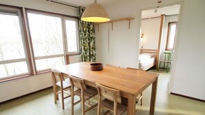 A dining area with a wooden table and chairs, a hanging lamp, and a view of a bedroom with a bed and a chair. - Amsterdam Farm Lodge: cosy holliday home (Amsterdam)