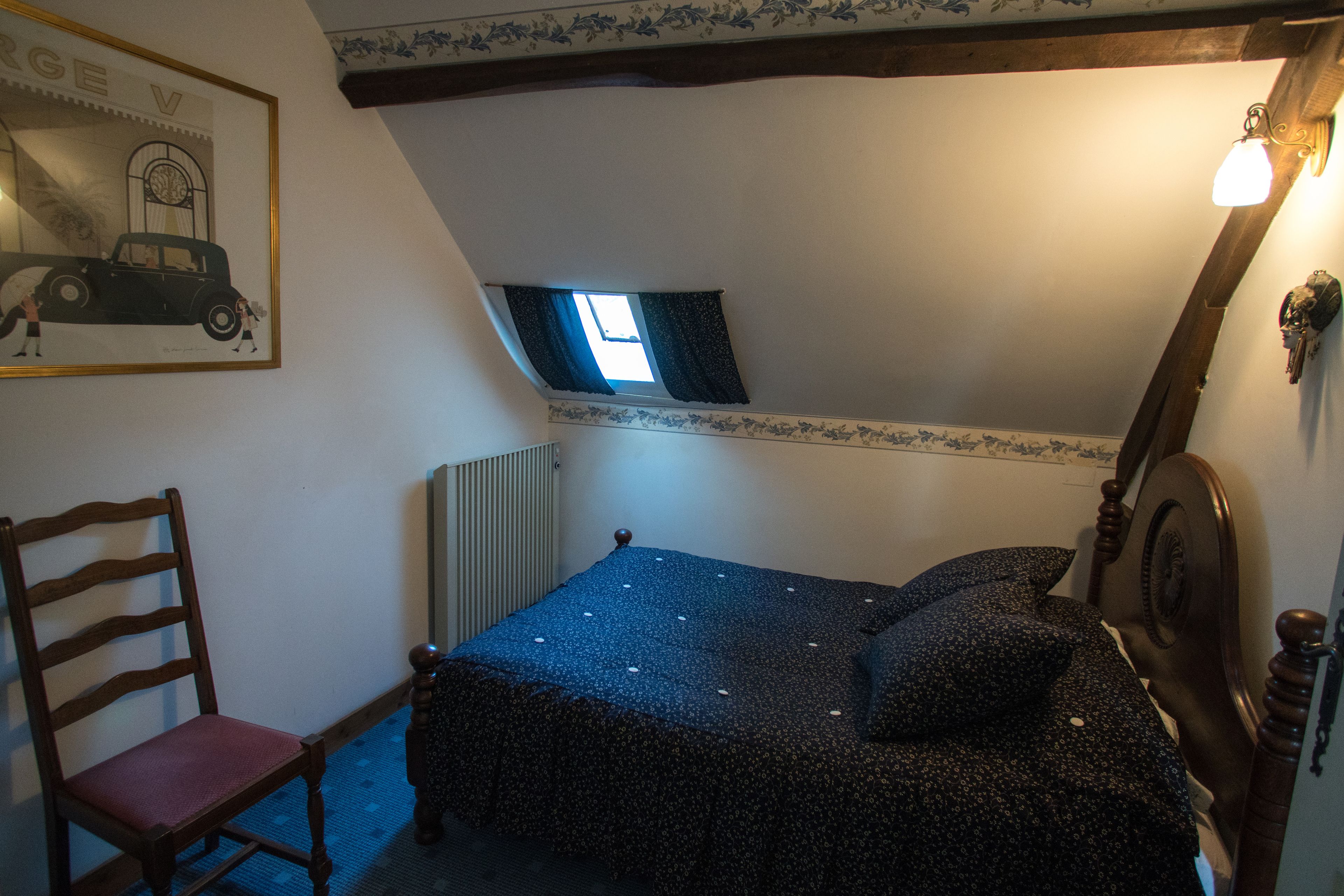 Un dormitorio con una cama, una silla, un radiador, una ventana y un aplique de pared.