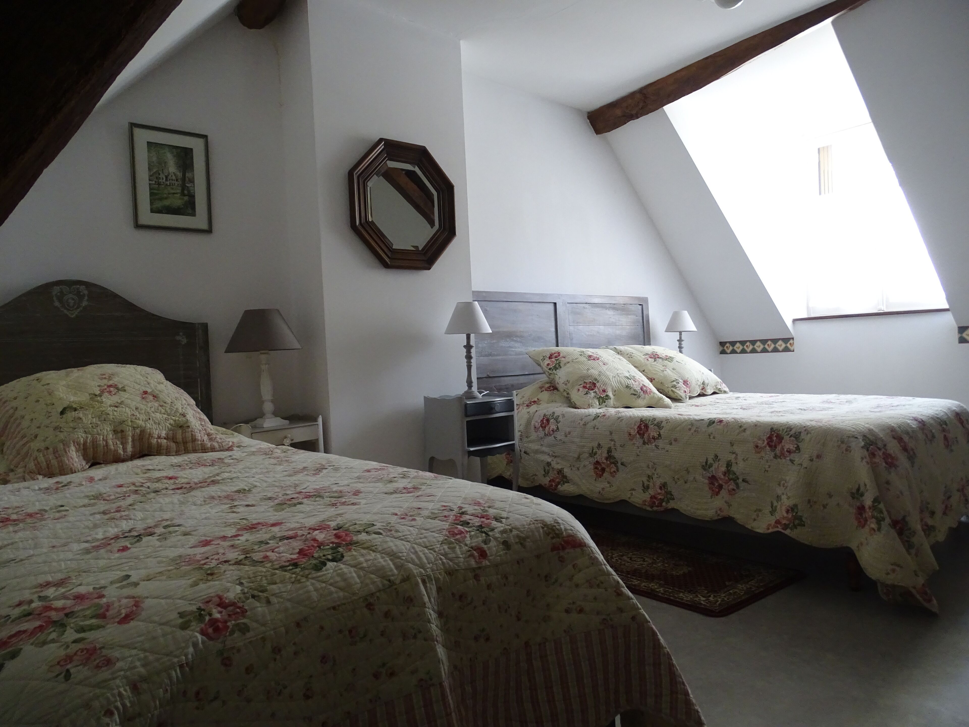 A bedroom with two beds, a wooden headboard, a nightstand, a lamp, a mirror, and a skylight.