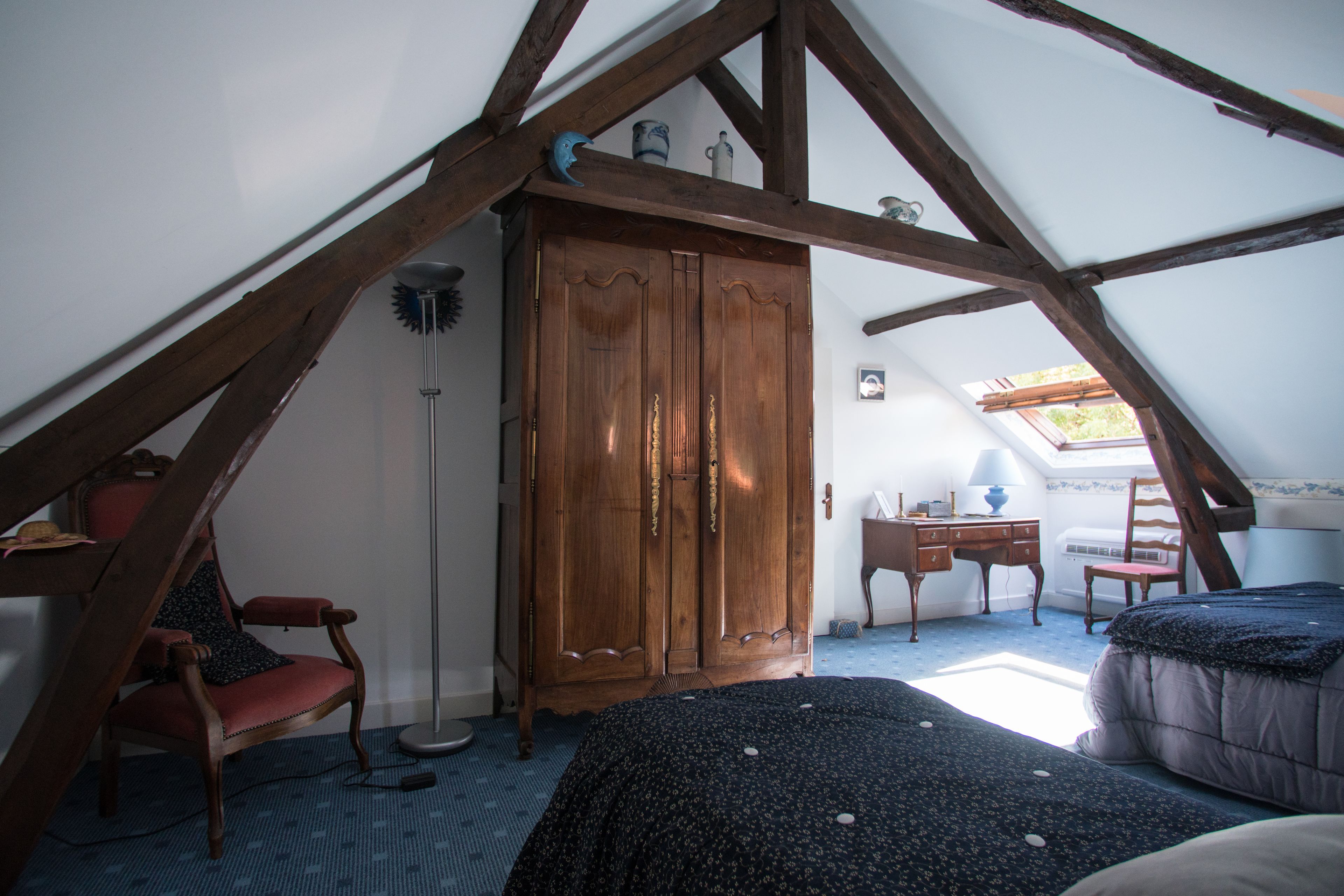 A bedroom with a sloped ceiling, wooden wardrobe, two chairs, a desk, and a bed.