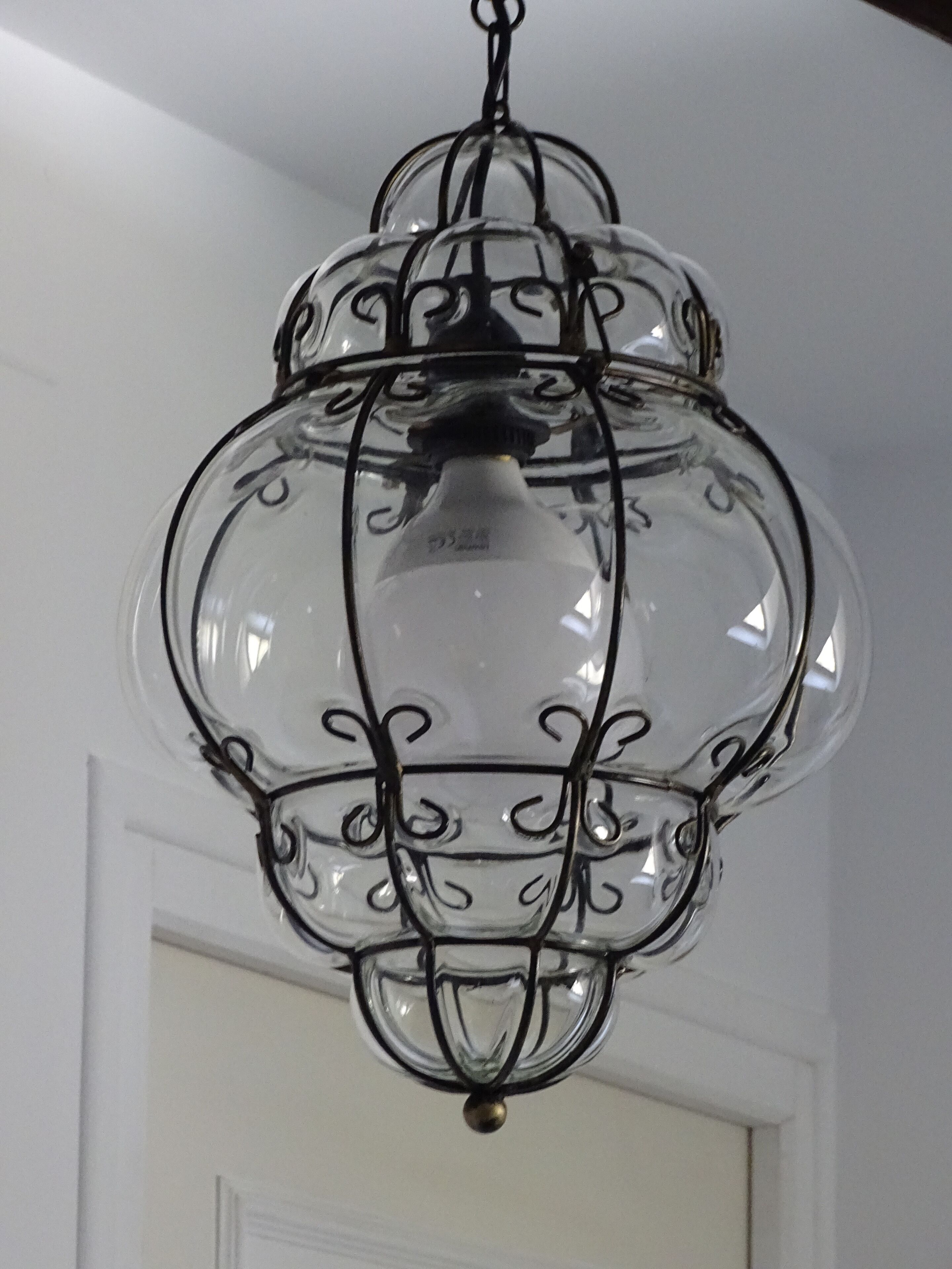 Een transparante glazen kroonluchter met een zwart metalen frame en één lamp.