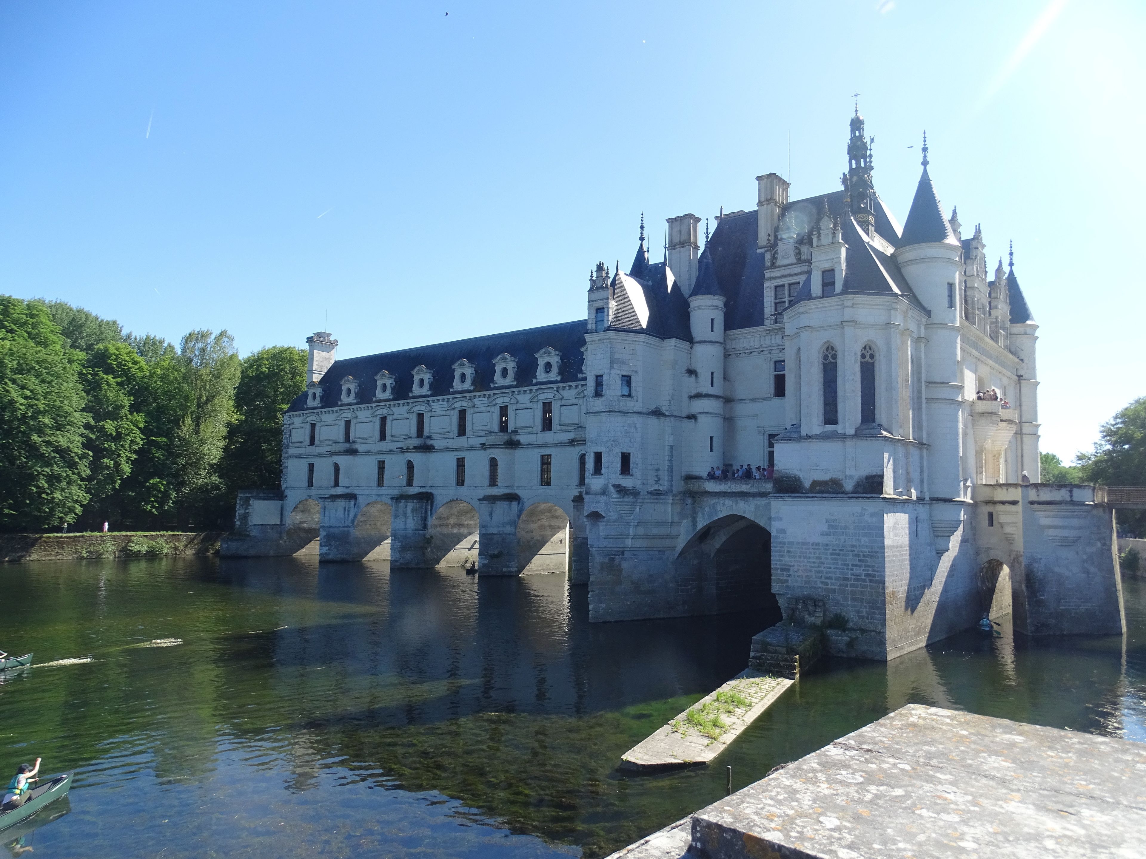 A historic building with a large arched bridge over a river, surrounded by lush greenery.