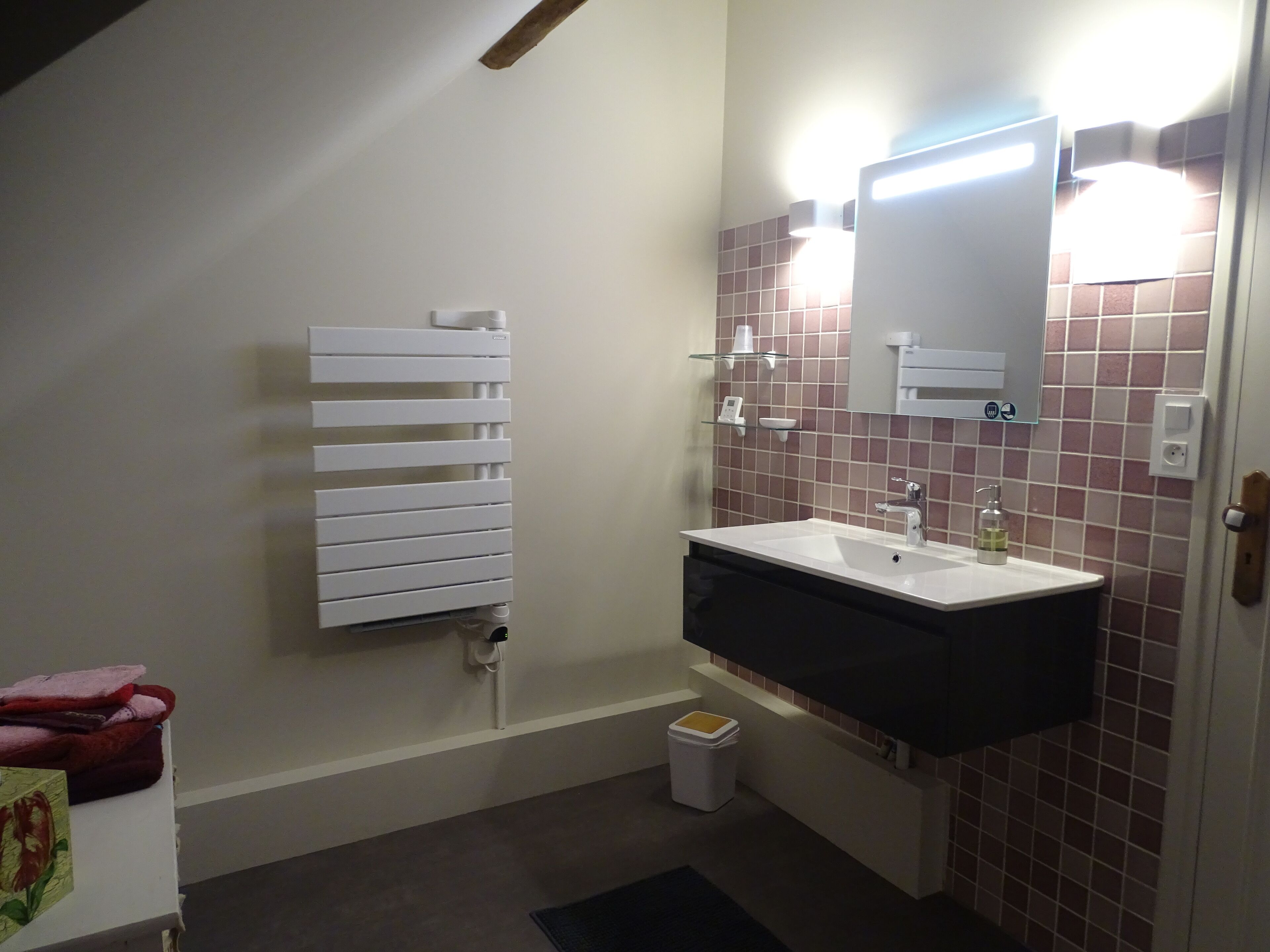 Un baño con un radiador blanco, un lavabo con espejo y un cubo de basura.