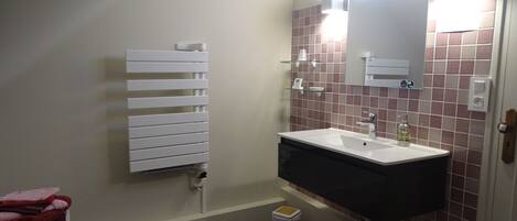 Un baño con un radiador blanco, un lavabo con espejo y un cubo de basura.