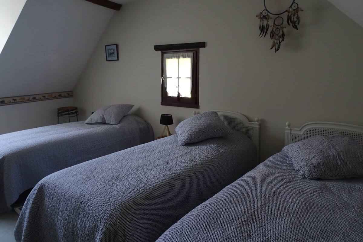 Een slaapkamer met twee bedden, een raam, een dromenvanger en een klein tafeltje.