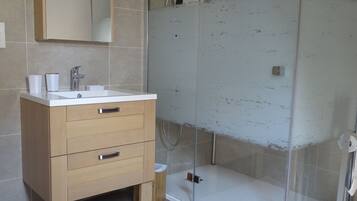 A modern bathroom with a glass-enclosed shower, a wooden vanity with drawers, and a mirror above the sink.