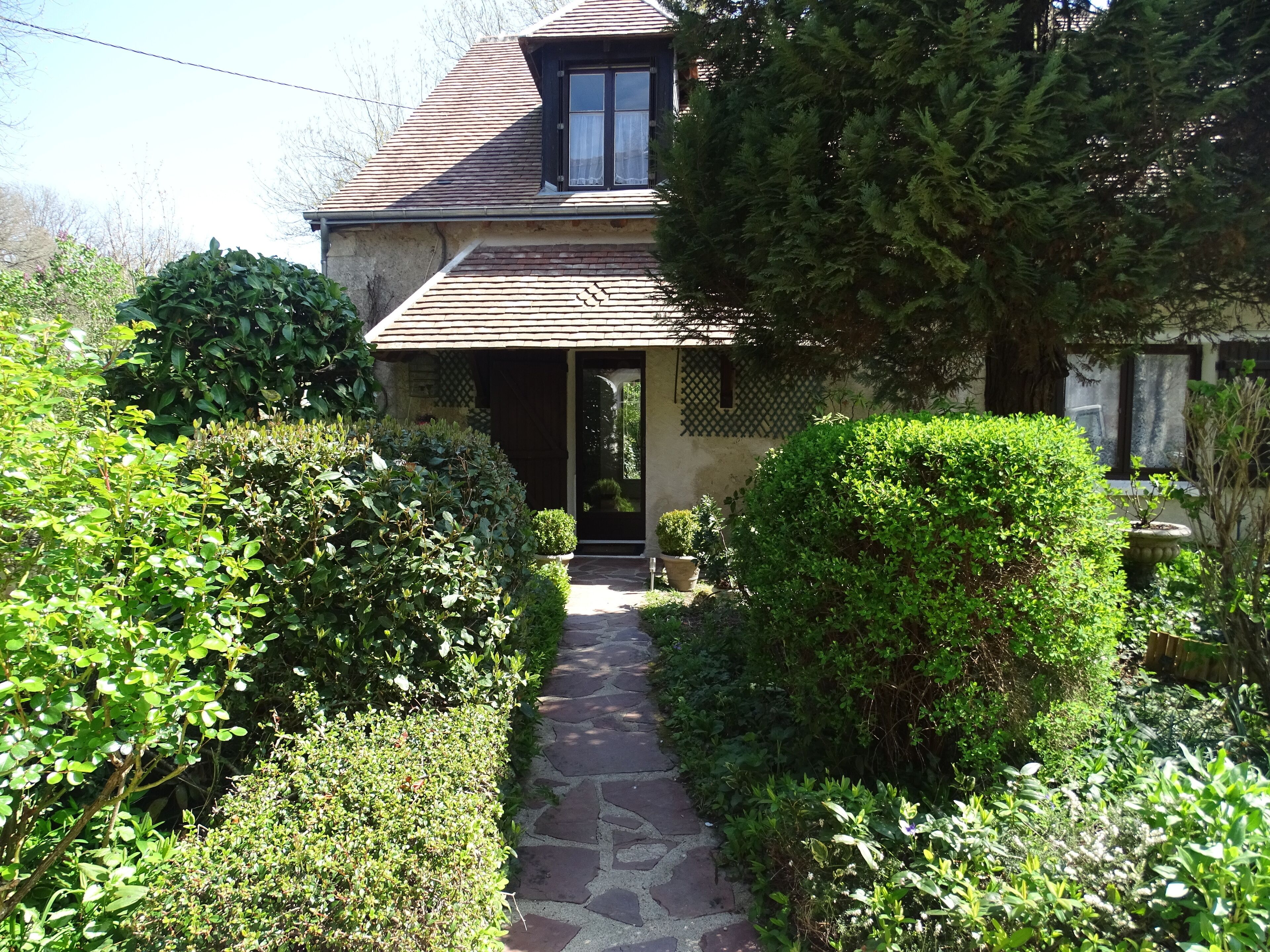 Un chemin de pierres mène à une maison avec un toit en tuiles et une fenêtre.