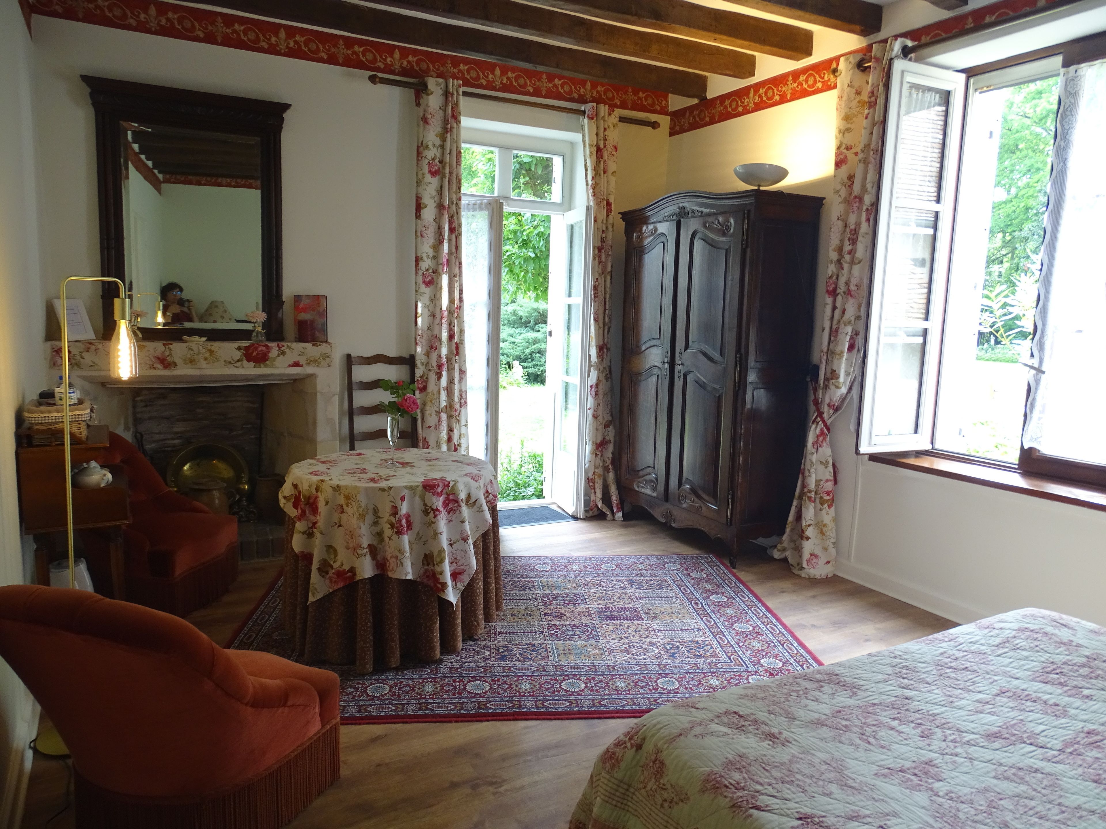 A room with a fireplace, a table with a floral tablecloth, a wardrobe, and a large window with curtains.