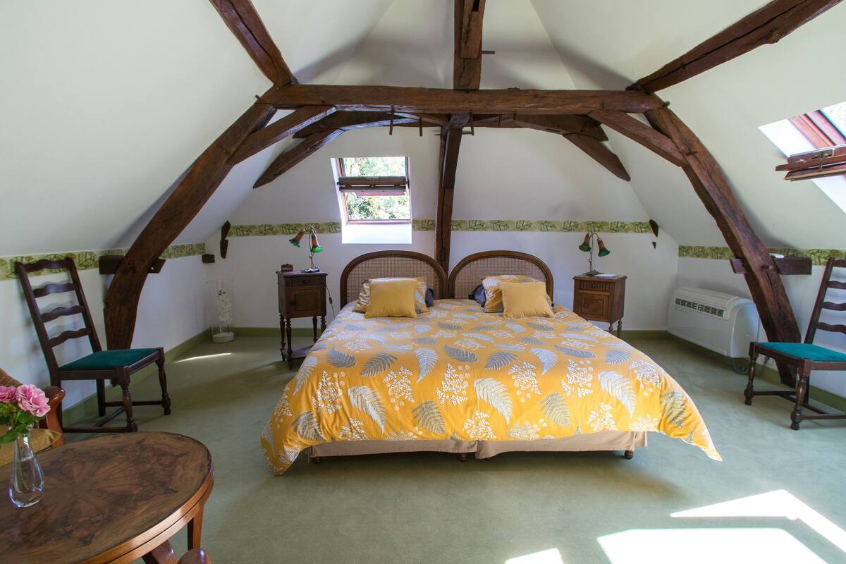Een slaapkamer met een schuine plafond, een bed met een bloemenprint sprei, twee nachtkastjes met lampen, en een raam dat natuurlijk licht biedt.