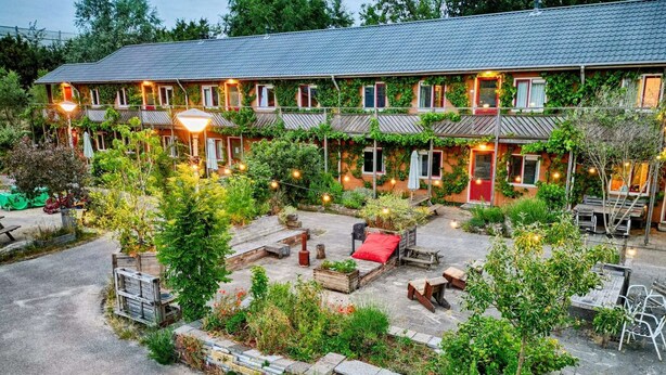 A two-story building with a covered outdoor seating area, multiple windows, and a red door. - Amsterdam Farm Lodge: group accommodation (Amsterdam)