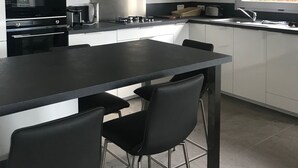 Una cocina moderna con una isla central, taburetes negros, electrodomésticos de acero inoxidable y un ventanal con vistas a zonas verdes.