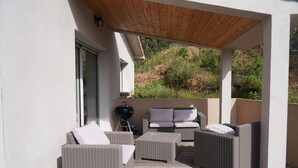 Un patio al aire libre con mobiliario de mimbre, una parrilla y vistas a una colina.