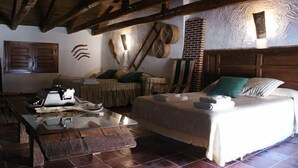 A rustic room with a wooden ceiling, a bed with a white bedspread, a wooden coffee table, and a brick wall with a textured design. - Tío Emilio Rural House for 15 people (Bienservida)