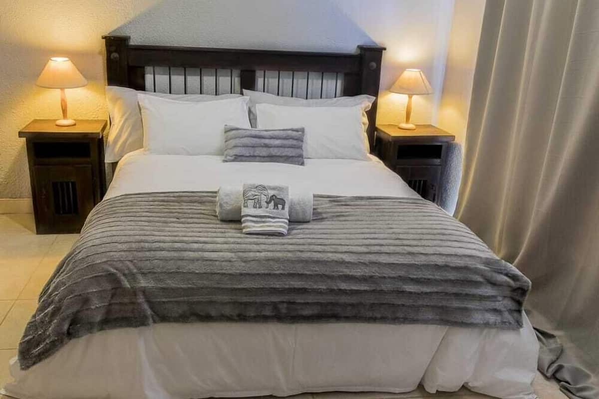 Una cama bien hecha con una colcha a rayas y una toalla con diseño de caballo, flanqueada por dos lámparas de noche en mesitas auxiliares iguales.