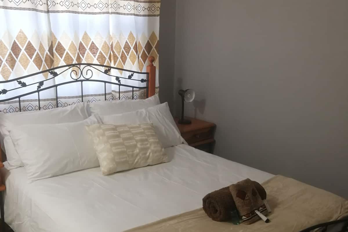 Una cama bien hecha con un cabecero estampado, una lámpara de noche y un bolso marrón sobre la cama.
