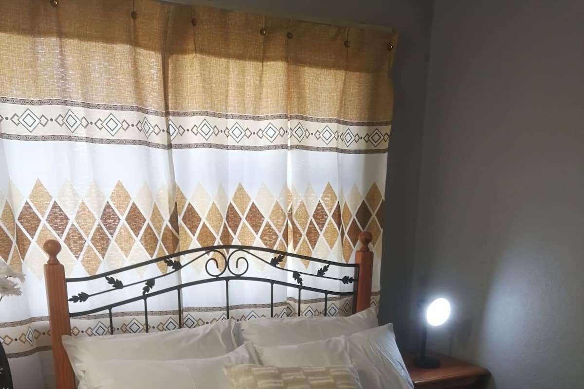 Una cama bien hecha con cabecera, lámpara de noche y un cojín decorativo.