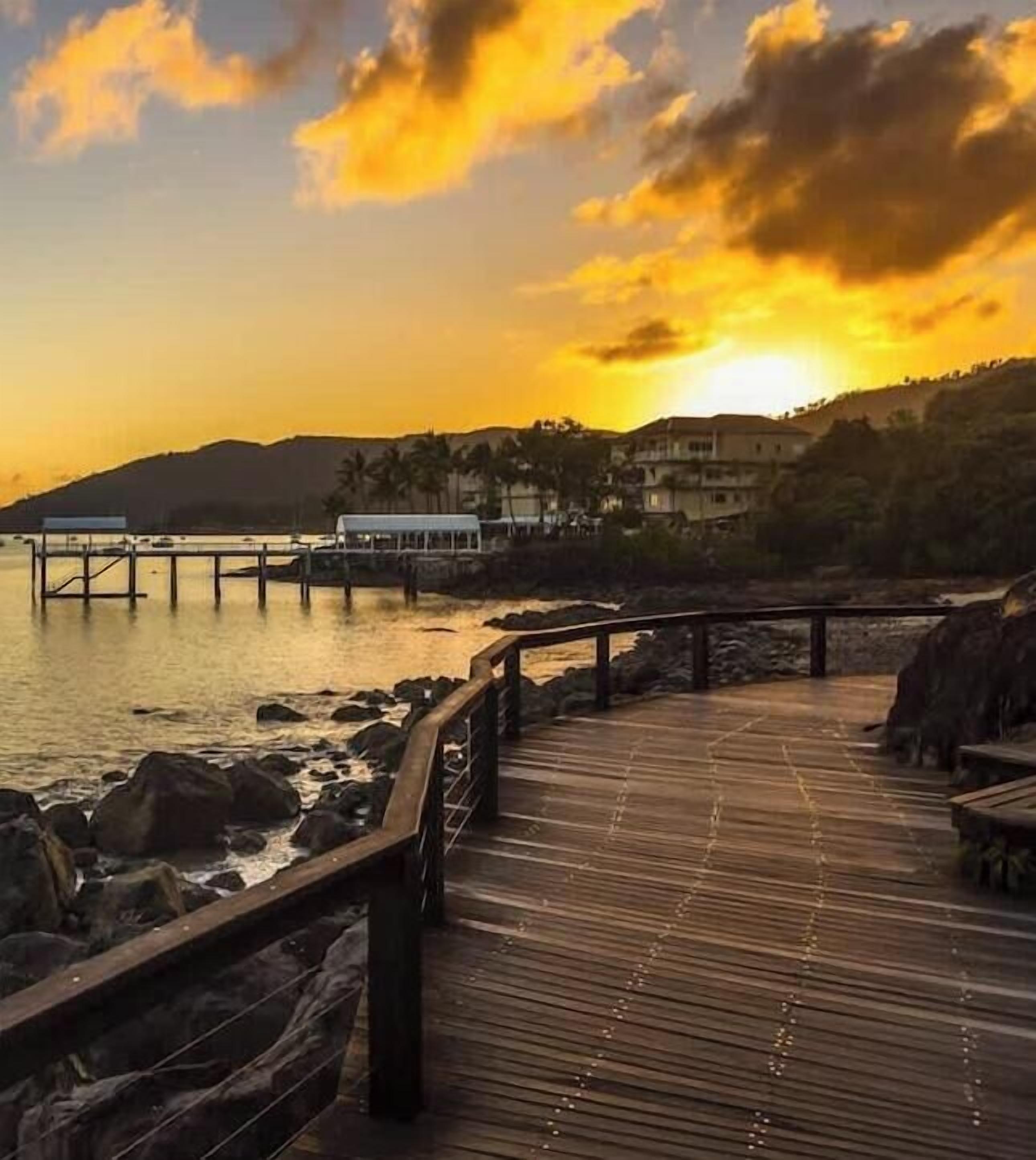 Une jetée en bois s’étendant sur des eaux calmes, avec un coucher de soleil en arrière-plan.
