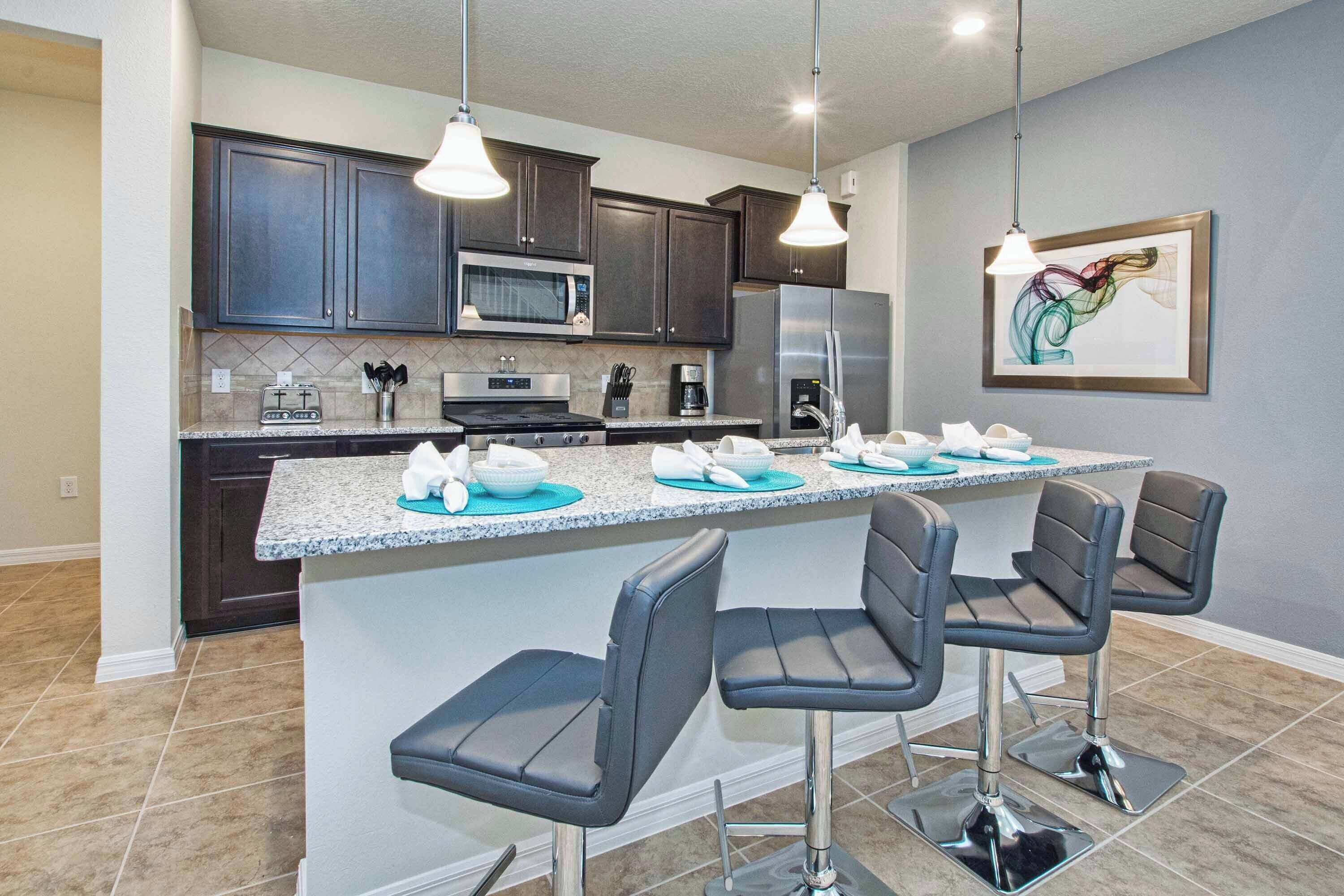 A modern kitchen with dark cabinets, a microwave, a refrigerator, and a bar area with three bar stools.
