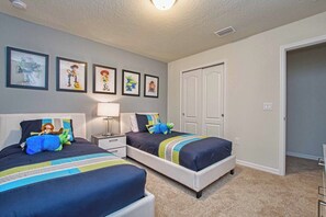 A bedroom with two beds, a nightstand, a lamp, and framed pictures on the wall.