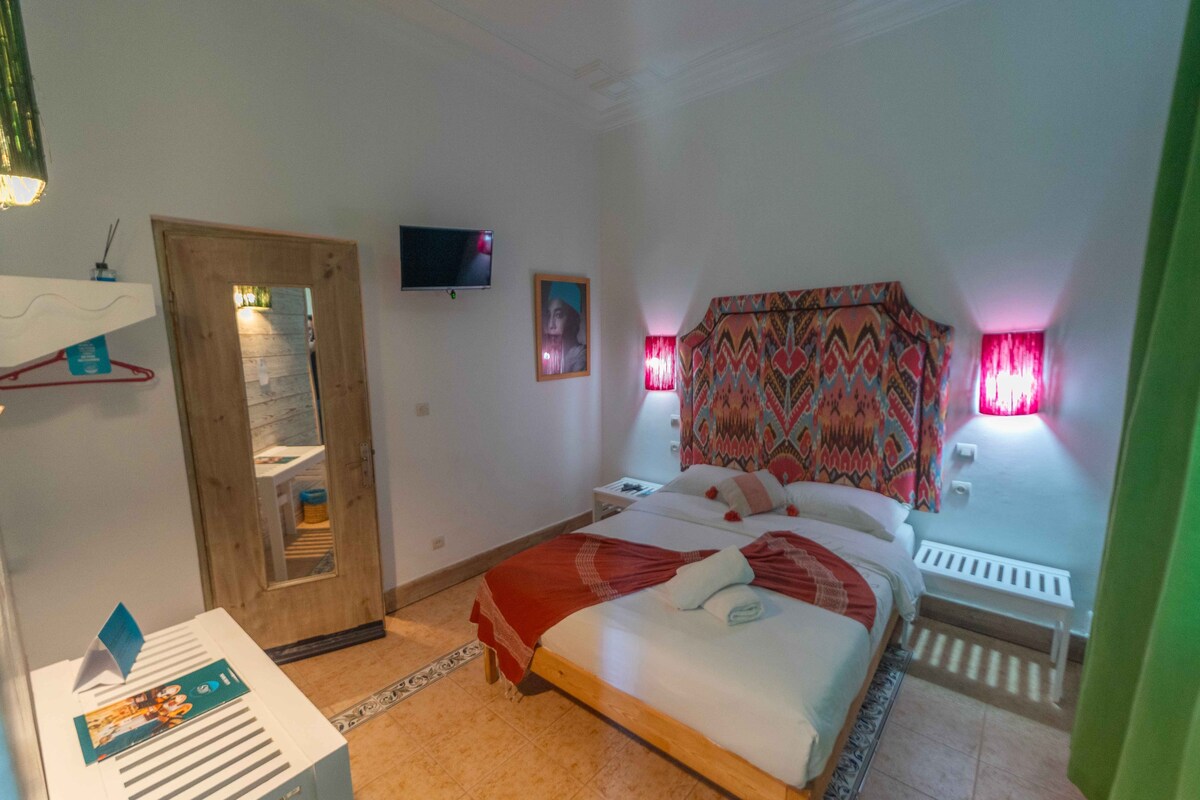 A hotel room with a bed, a television, a mirror, a door, and a window with curtains.