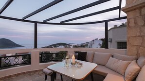 A terrace with a table and seating, overlooking a coastal landscape.