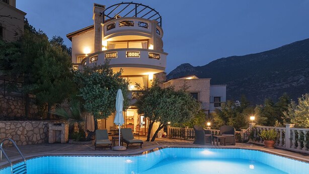 A multi-story building with a swimming pool, outdoor seating, and a mountainous backdrop.