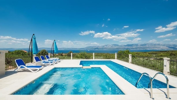 A rooftop pool with blue chairs and umbrellas, surrounded by a white fence, overlooking a mountainous landscape. - Villa Agape - Three Bedroom Villa with Swimming Pool (Mirca)