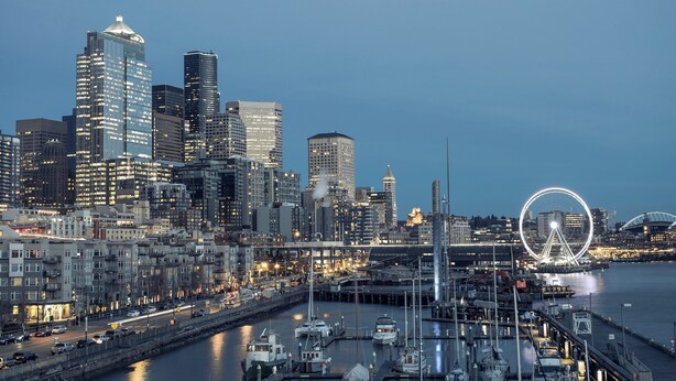 A waterfront cityscape with modern high-rise buildings, a marina with boats, and a prominent circular light structure. - Modern Studio in the Heart of the City II (Seattle)