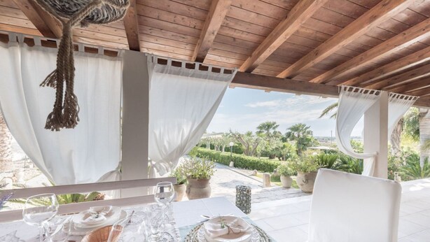 Comedor con una mesa preparada para cuatro personas, mantel blanco y vistas a un jardín.