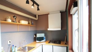 Una cocina compacta con microondas, estufa y lavamanos. Hay estantes sobre la encimera con frascos y botellas.