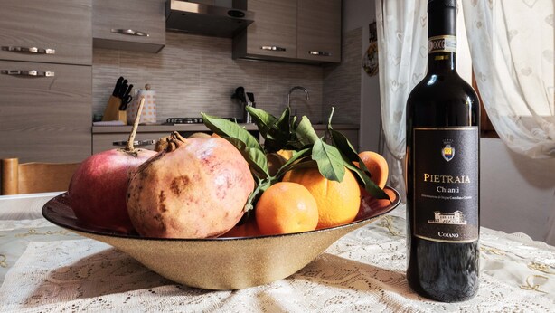 A bowl of fruit and a bottle of wine on a table in a kitchen. - Casa Erika, relax in Tuscany   (Partino)