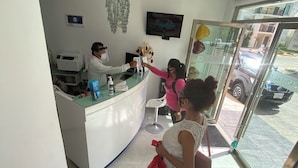 A reception area with a counter, a chandelier, a television, and a glass door leading outside. - Hotel Quinta Santa Anita (Playa del Carmen)