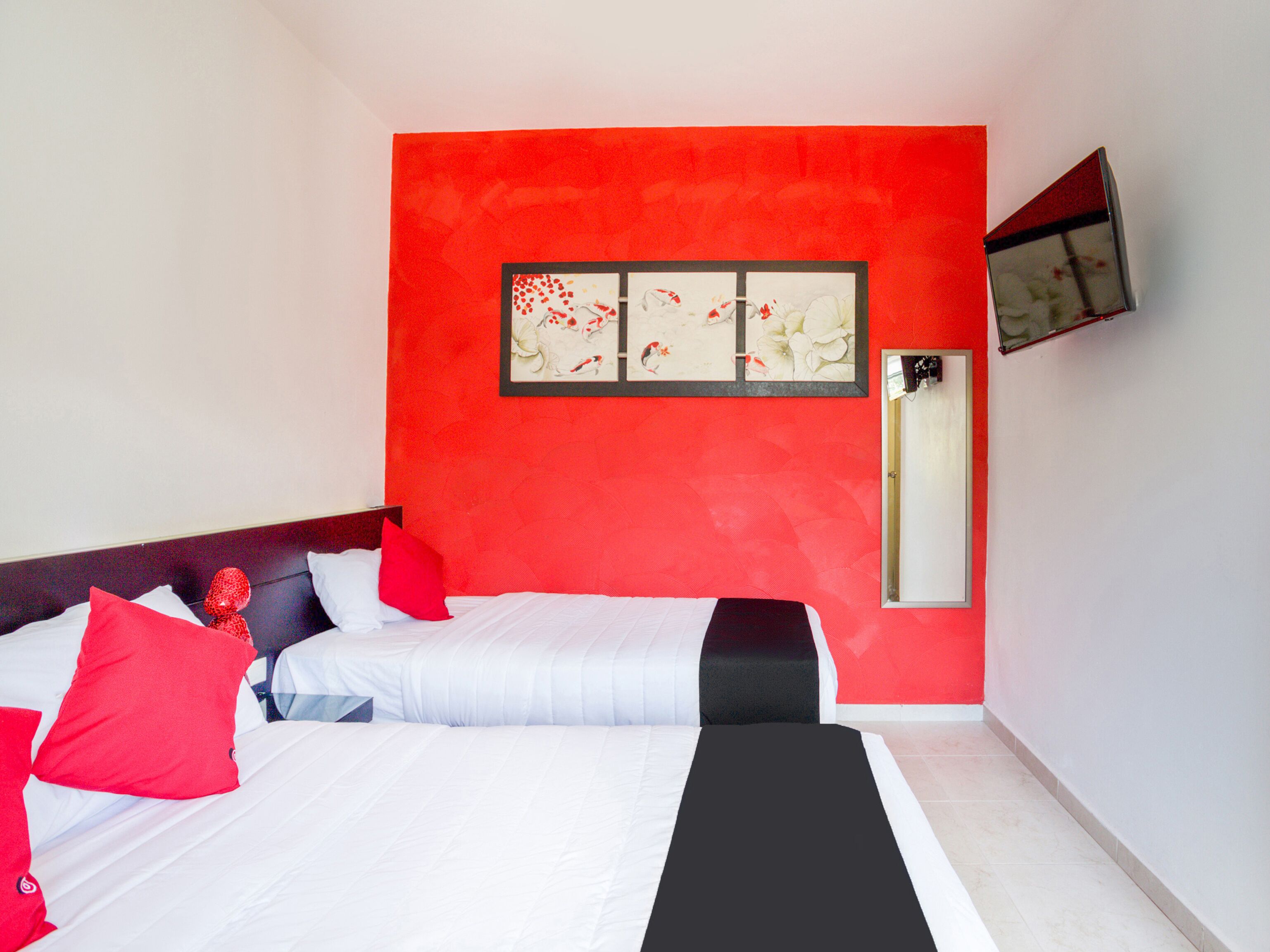 Una habitación de hotel con una pared de acento roja, una cama con ropa de cama blanca y negra, y una obra enmarcada sobre la cama.