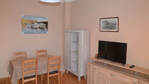 A dining area with a table and chairs, a television on a wooden stand, and two framed pictures on the wall. - Accommodation Junonia Marítimo 1 (Playa de Santiago)
