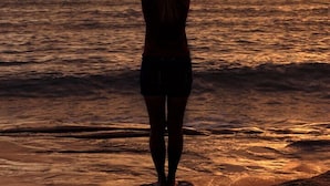 En person står på en strand og ser ud over havet i solnedgangen.