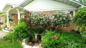 Et hus med murstensfacade, en overdækket veranda og en have med forskellige planter og blomster.
