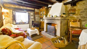A cozy living room with a stone fireplace, wooden furniture, and a television. - House of integral rent in the center of Cantabria. 8 people (La Serna de Iguña)